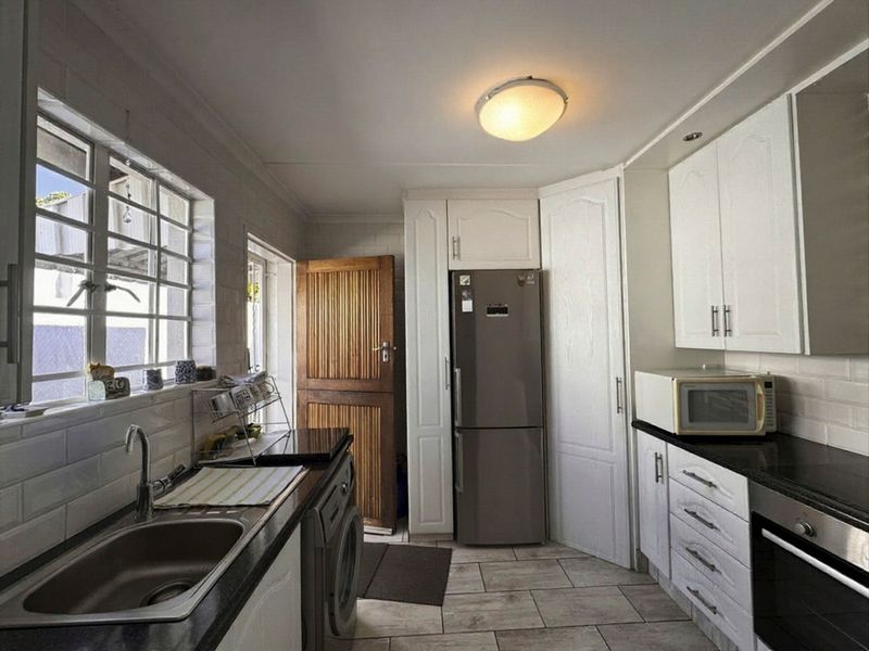 A functional kitchen featuring white cabinetry, dark stone countertops, built-in oven, and tiled flooring with direct access to an exterior door.