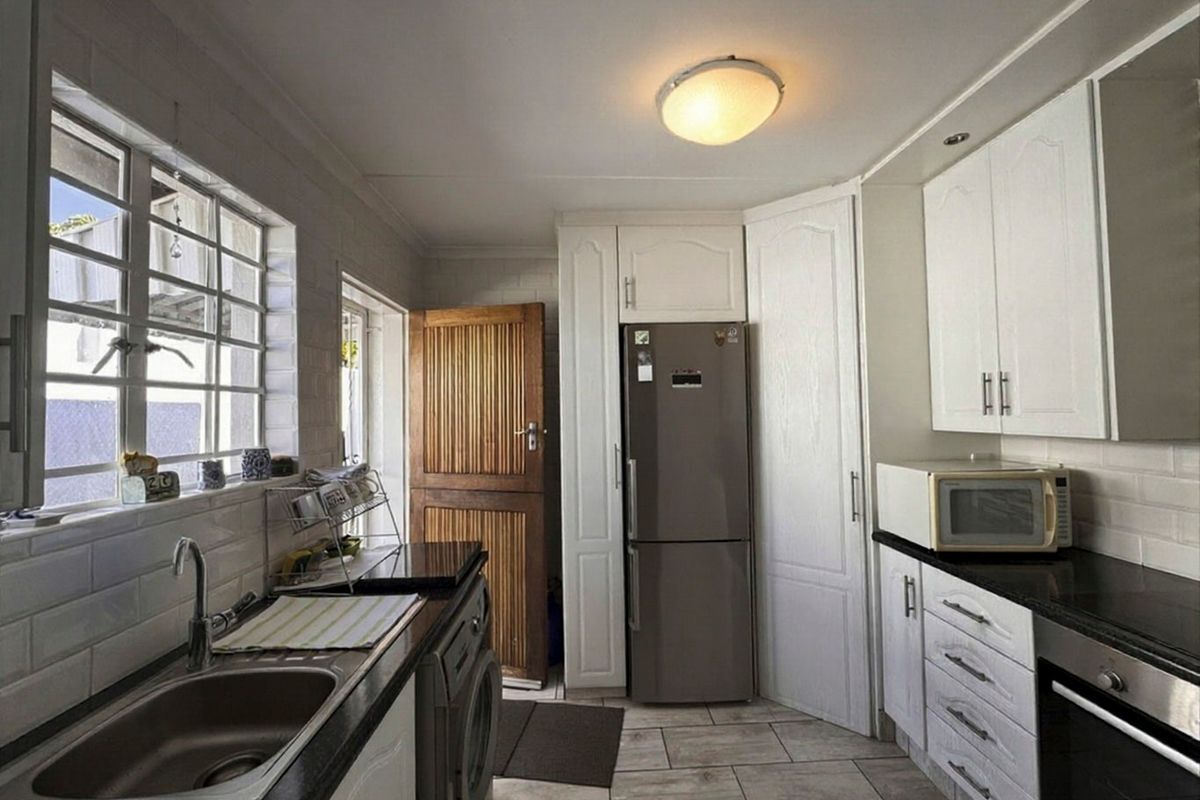 A functional kitchen featuring white cabinetry, dark stone countertops, built-in oven, and tiled flooring with direct access to an exterior door.