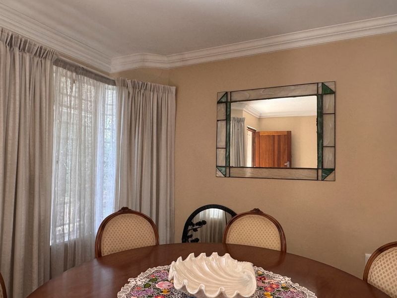 A dining room area featuring neutral wall tones, decorative cornice detailing, and large windows with installed curtain tracks.