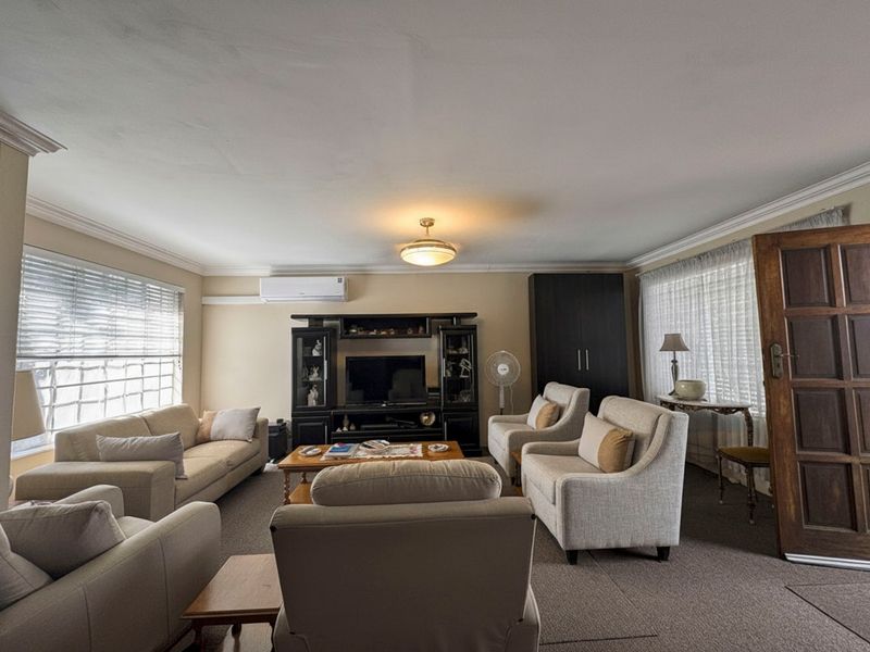 A spacious living room featuring neutral carpeting, split-system air conditioning, and classic cornice detailing, offering a comfortable and functional layout.