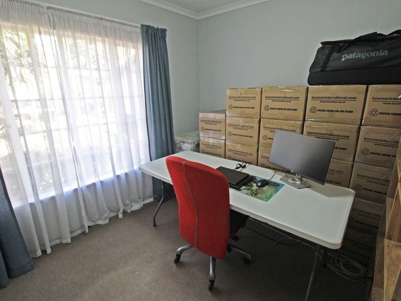 A functional bedroom space featuring carpeted flooring and a large window, currently utilized as a home office area.