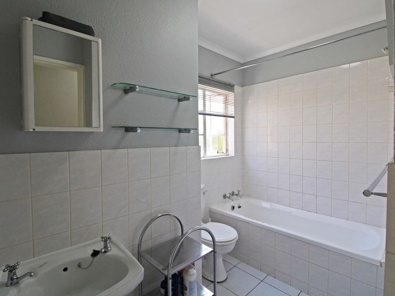 A functional bathroom featuring a bathtub, pedestal basin, and wall-mounted mirror cabinet with neutral tiled finishes.