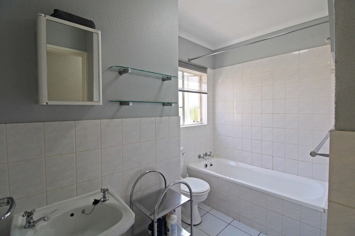 A functional bathroom featuring a bathtub, pedestal basin, and wall-mounted mirror cabinet with neutral tiled finishes.