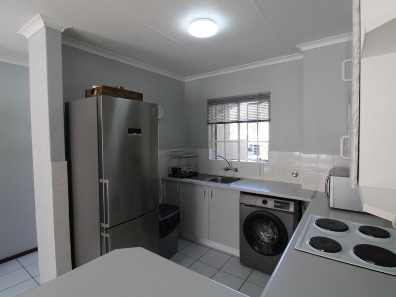 Compact kitchen featuring built-in cabinetry, tiled backsplash, electric hob, and tiled flooring, providing a functional workspace with integrated appliance connections.