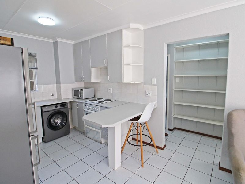 A functional kitchen featuring built-in cabinetry, tiled flooring, an electric stove, a breakfast bar, and an adjacent walk-in pantry with built-in shelving.