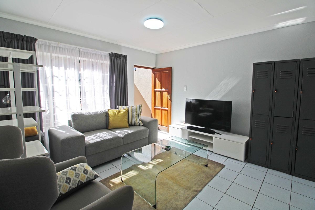 A bright living room featuring tiled flooring, a ceiling light fixture, and access to an outdoor area through a sliding glass door.