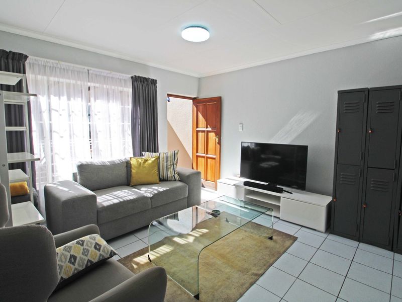 A bright living room featuring tiled flooring, a ceiling light fixture, and access to an outdoor area through a sliding glass door.