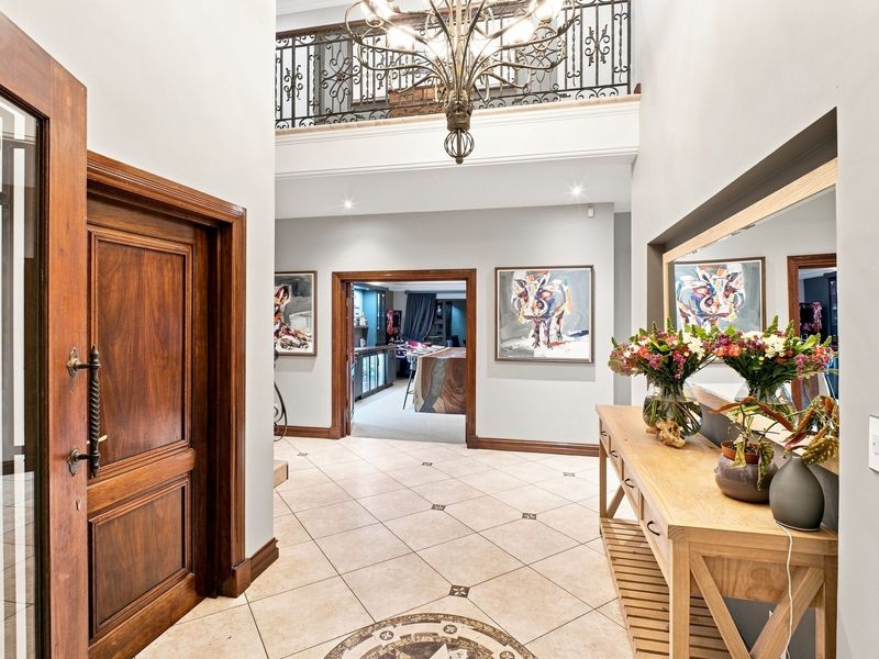 Spacious double-volume entrance hall featuring tiled flooring, a decorative wrought iron balustrade, and a grand chandelier, leading into the main living areas.
