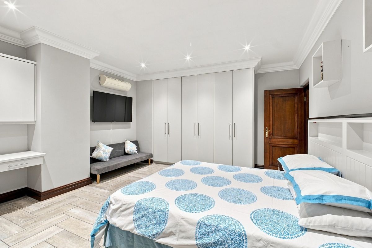 A well-maintained bedroom featuring extensive built-in cupboards, recessed lighting, crown molding, and tiled flooring, providing a clean and functional living space.