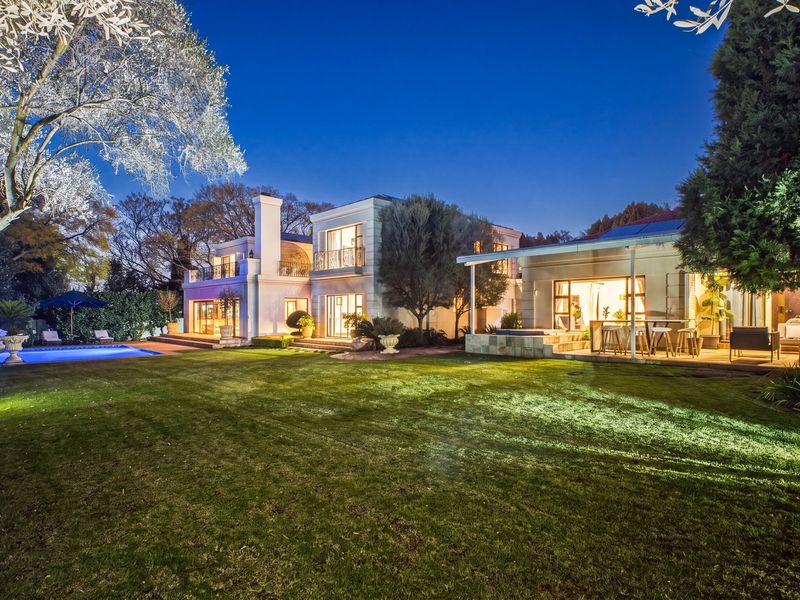 A beautifully illuminated rear exterior view featuring a spacious lawn, a swimming pool, and a covered patio area attached to the main residence.