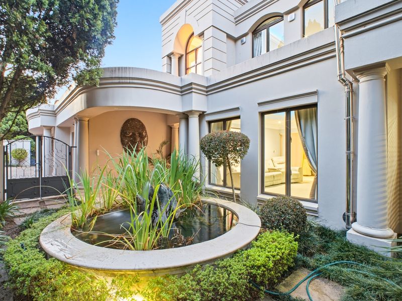 A well-maintained rear exterior featuring a stone water fountain, covered patio area, and classic architectural columns.