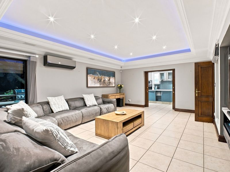 Spacious living room featuring a recessed tray ceiling with ambient LED lighting, tiled flooring, and direct access to an outdoor area.