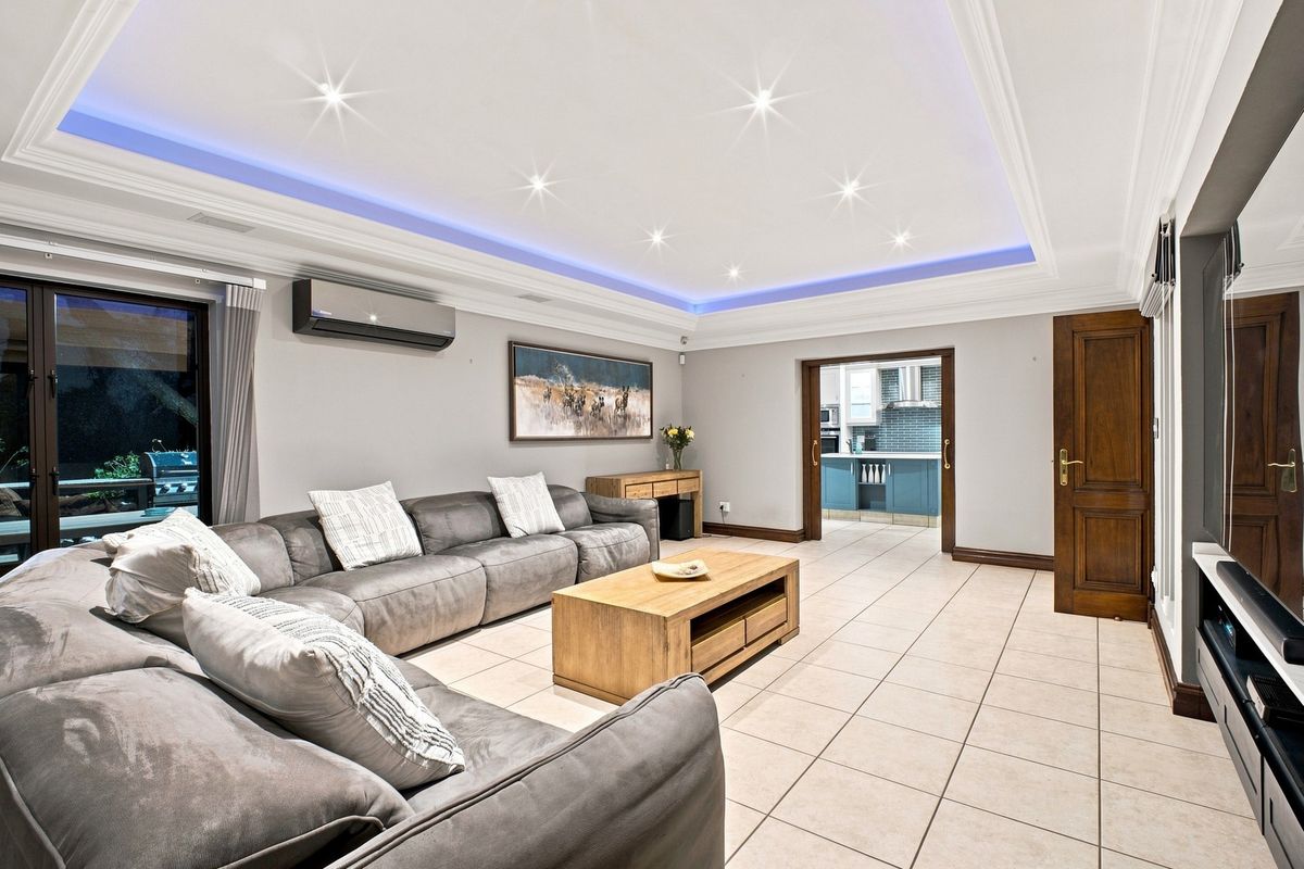 Spacious living room featuring a recessed tray ceiling with ambient LED lighting, tiled flooring, and direct access to an outdoor area.