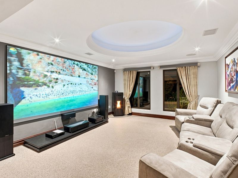 A well-appointed cinema room featuring a large projection screen, recessed ceiling dome with ambient lighting, and a built-in pellet stove.