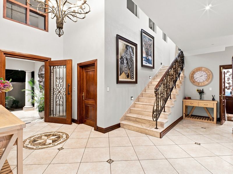 Grand double-volume entrance hall featuring a stone staircase with ornate wrought iron railing, decorative floor tiling, and a feature chandelier.