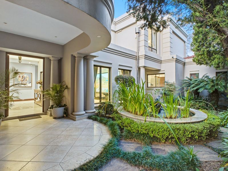 A well-maintained rear patio area featuring stone tiling, decorative columns, and a landscaped garden with a built-in water feature.