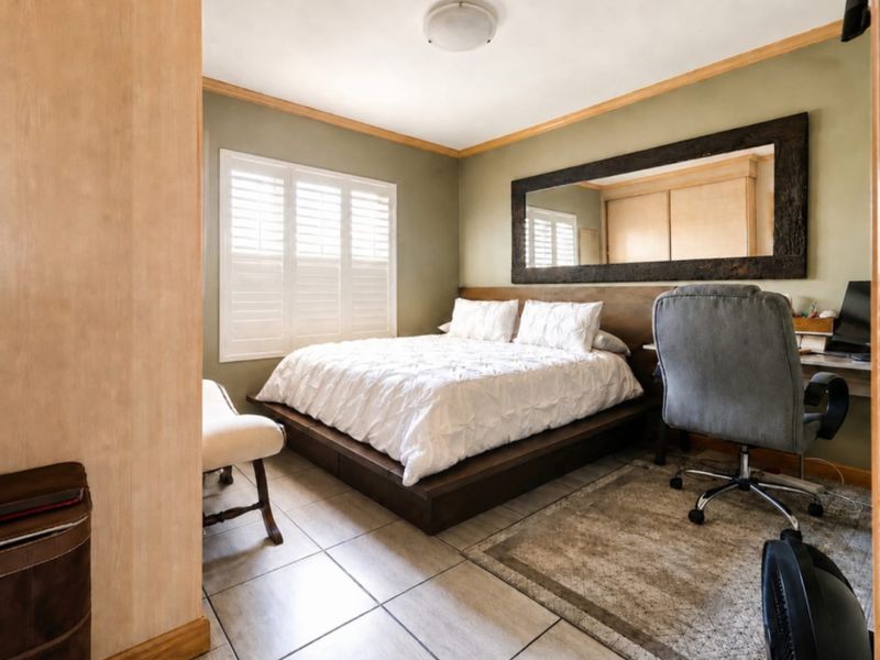 A well-maintained bedroom featuring tiled flooring, plantation shutters, and a built-in wardrobe, offering a functional and comfortable living space.