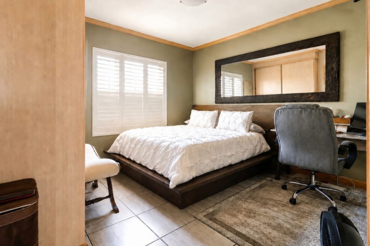 A well-maintained bedroom featuring tiled flooring, plantation shutters, and a built-in wardrobe, offering a functional and comfortable living space.