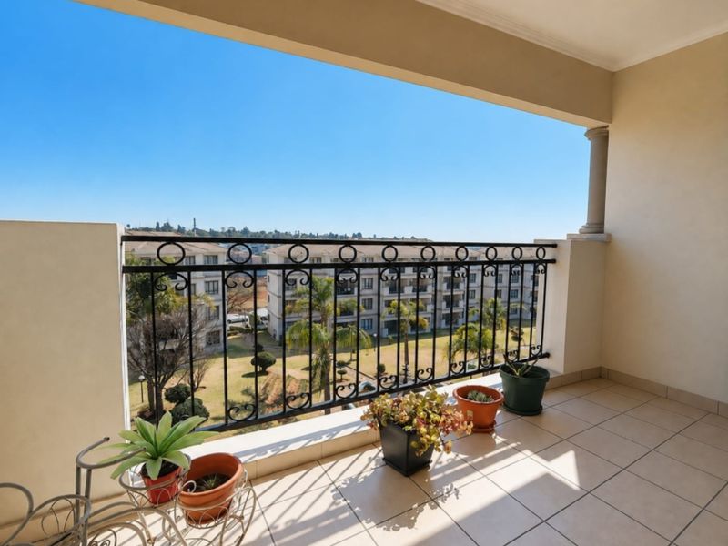 A spacious covered balcony featuring tiled flooring and a decorative wrought iron balustrade, offering pleasant views over the complex grounds.