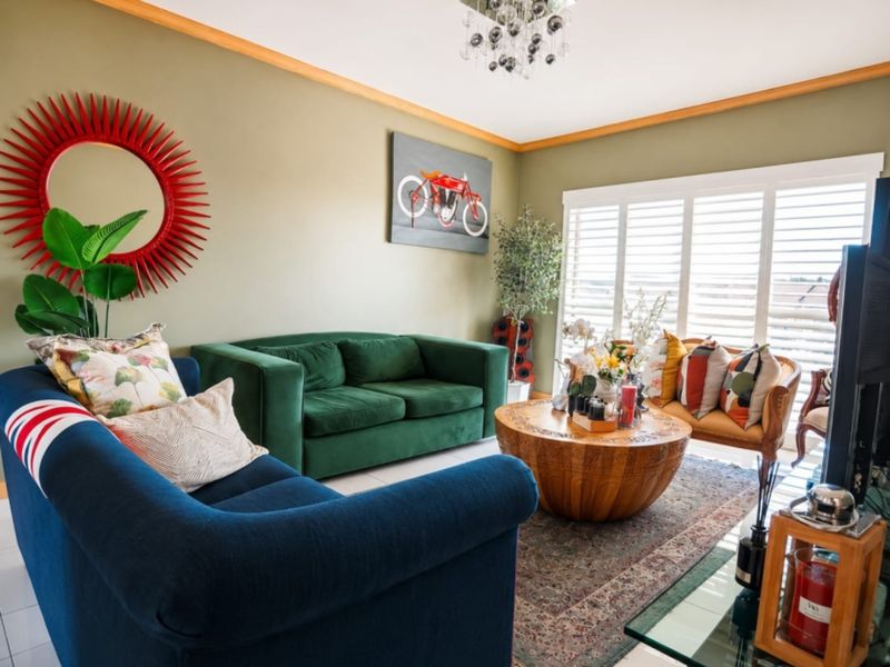 A well-maintained living room featuring elegant crown molding, tiled flooring, and plantation shutters that allow for adjustable natural light.