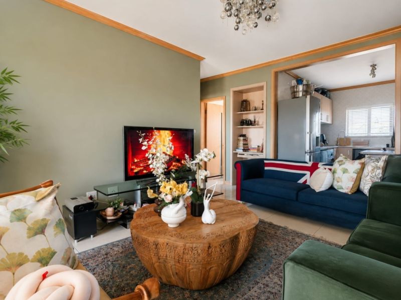 Open plan living area featuring tiled flooring, crown molding, and built-in shelving, with an adjacent kitchen visible in the background.
