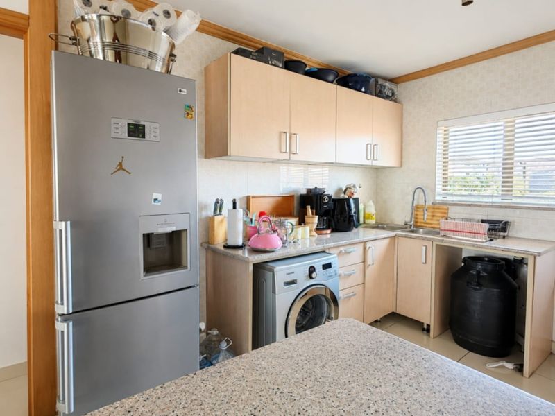 A functional kitchen featuring light wood cabinetry, granite countertops, and a stainless steel sink, with space for integrated laundry appliances.