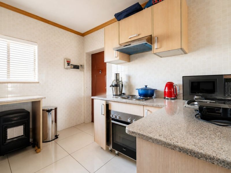 A functional kitchen featuring light wood cabinetry, granite countertops, built-in oven, electric hob, and tiled finishes throughout.