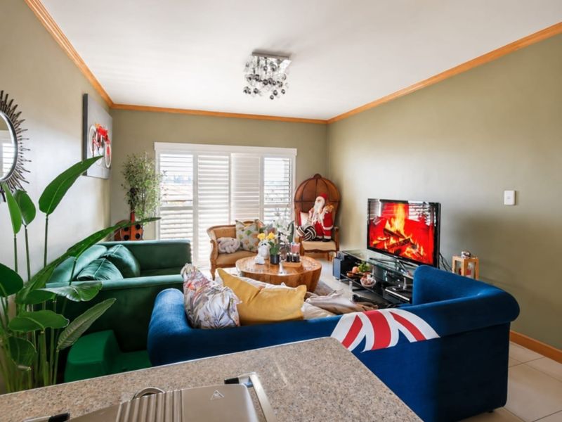 A comfortable living room featuring tiled flooring, crown molding, and plantation shutters, providing a bright and inviting space for relaxation.