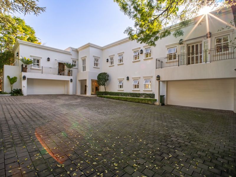 A well-maintained front elevation featuring a spacious paved driveway, double garage, and upper-level balconies with classic wrought iron railings.