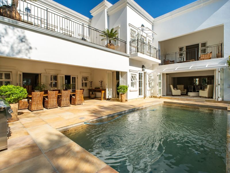 A luxurious outdoor pool area featuring a stone patio, covered entertainment space, and elegant wrought iron balcony railings overlooking the swimming pool.