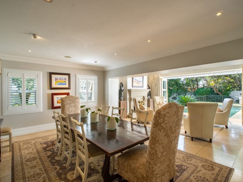 Spacious open-plan dining and living area featuring tiled floors, recessed lighting, plantation shutters, and a fireplace with direct access to the outdoor pool area.
