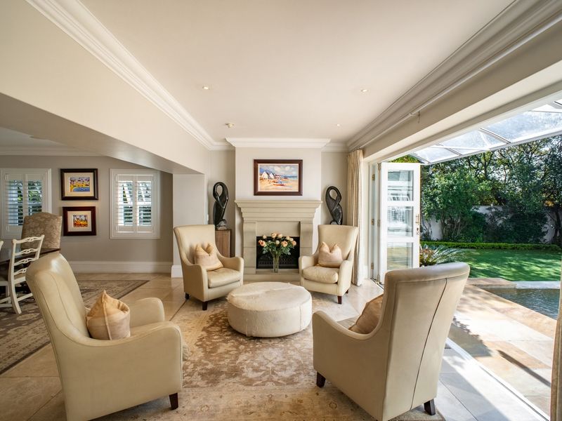 Elegant living room featuring a central fireplace, crown molding, and large bi-fold doors opening to a landscaped garden and pool area.