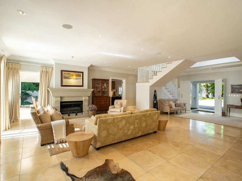 Spacious open-plan living area featuring a stone fireplace, elegant staircase, polished stone flooring, and abundant natural light from a skylight and entrance.