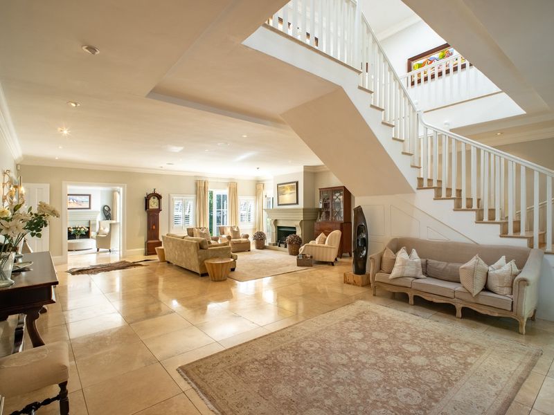 Spacious open-plan living area featuring elegant stone flooring, a grand staircase with a classic balustrade, and a central fireplace.