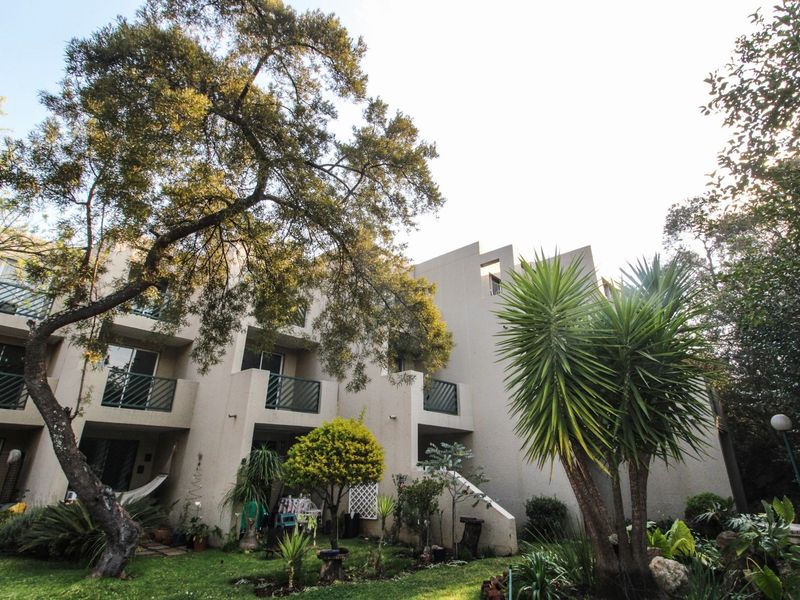 Rear view of a multi-story apartment building featuring private balconies, sliding glass doors, and a well-maintained garden area.
