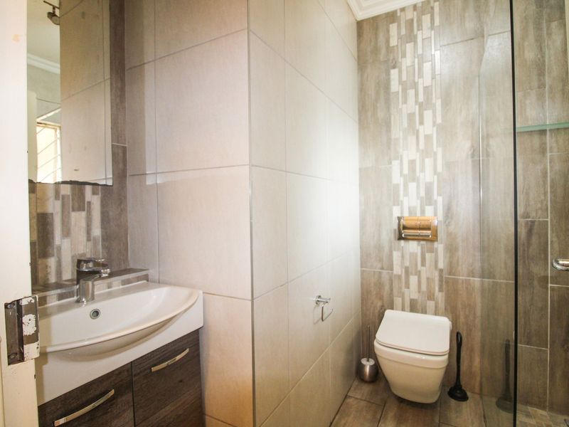 Modern bathroom featuring a vanity basin, wall-mounted toilet, and a glass-enclosed shower with decorative tiled accents.