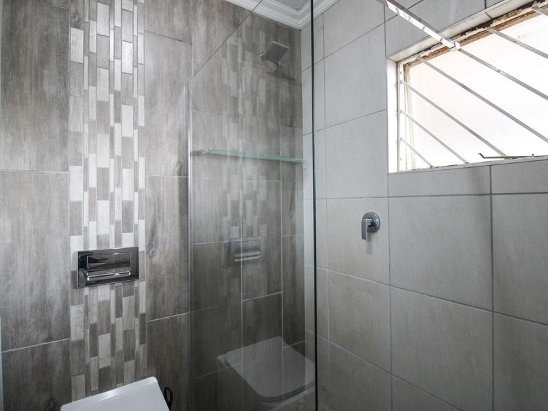 Modern bathroom featuring a glass-enclosed shower, contemporary wall-mounted flush plate, and neutral grey tiled finishes.