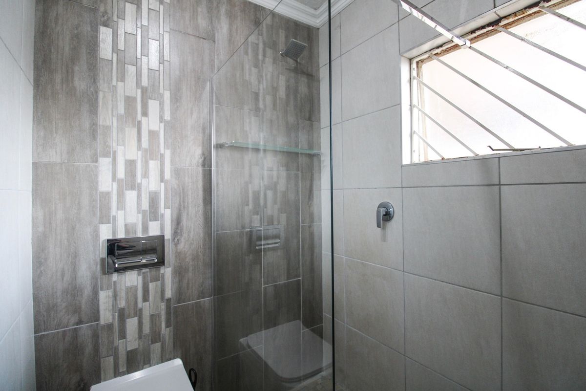 Modern bathroom featuring a glass-enclosed shower, contemporary wall-mounted flush plate, and neutral grey tiled finishes.