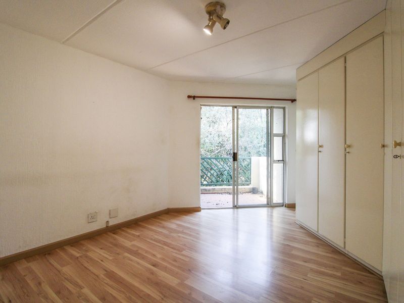An empty bedroom featuring laminate flooring, built-in cupboards, and a sliding glass door providing access to a balcony.