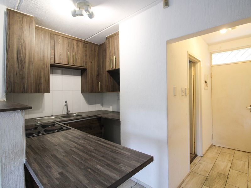 A compact kitchen featuring wood-look laminate countertops, built-in cabinetry, and an integrated electric hob, adjacent to the apartment entrance hallway.