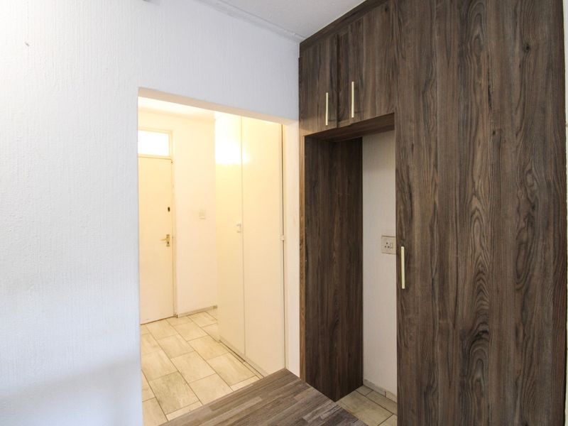 A clean hallway featuring built-in wooden cabinetry and light-colored floor tiles, providing a functional transition space within the apartment.
