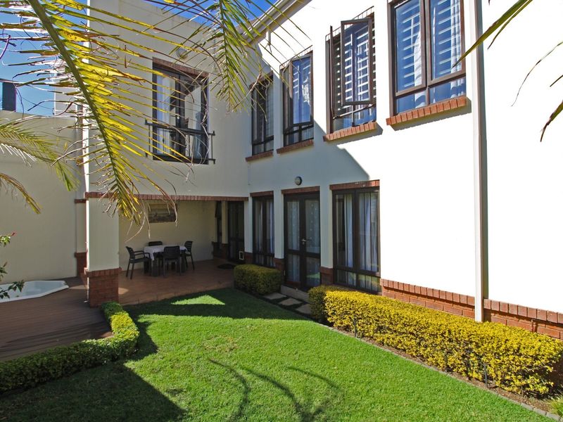 Rear exterior view featuring a covered patio, wooden decking with a built-in spa, and a well-maintained lawn area.