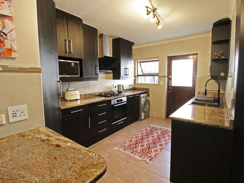 A well-appointed kitchen featuring dark wood cabinetry, granite countertops, a gas hob, built-in oven, and integrated sink with direct access to the exterior.