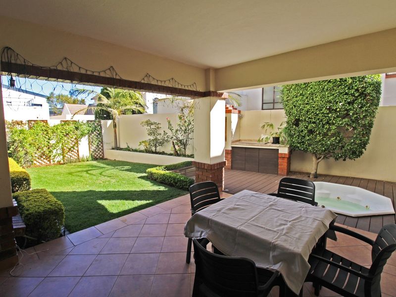 Covered patio featuring a built-in braai area, integrated spa, and direct access to a landscaped garden with lawn and retaining walls.