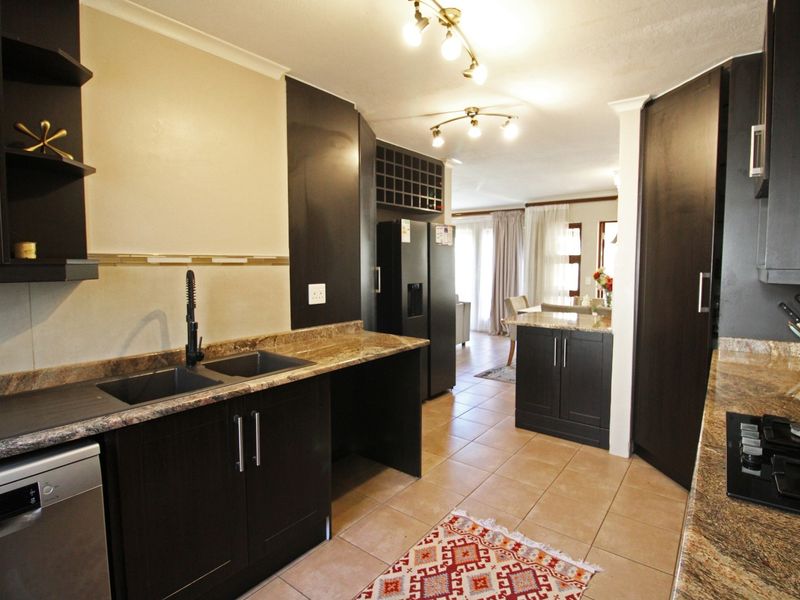 Modern kitchen featuring dark wood cabinetry, granite countertops, a gas hob, and a double sink, flowing into an open-plan living area.