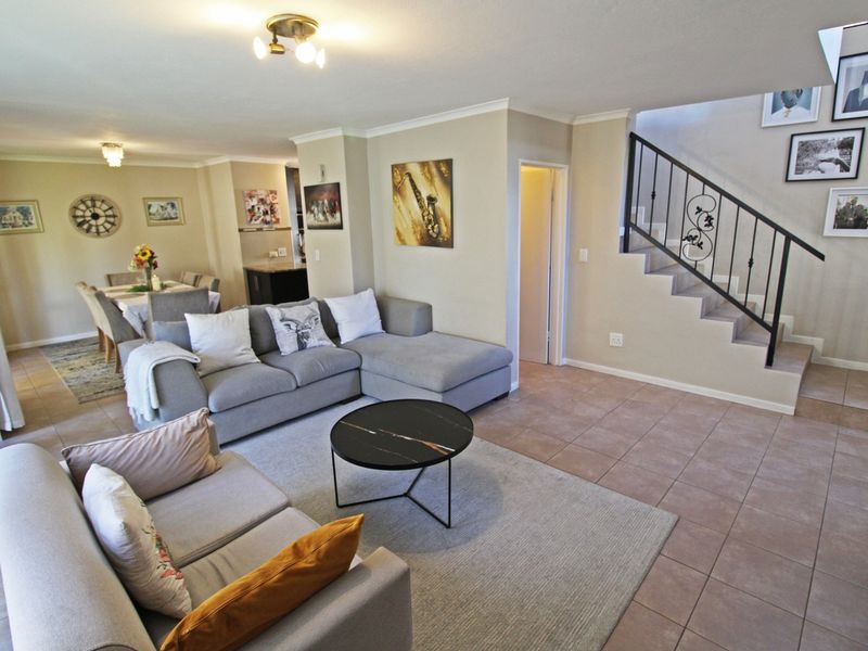 Spacious open-plan living and dining area featuring tiled flooring, a staircase with decorative wrought iron railing, and neutral wall finishes.