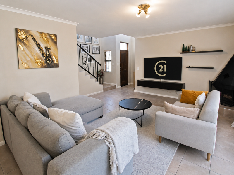 A well-maintained living room featuring tiled floors, a built-in fireplace, floating shelving, and a staircase with a decorative wrought iron railing.