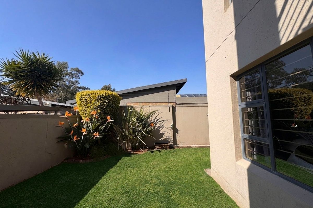 A well-maintained rear garden area featuring a manicured lawn, perimeter boundary walls with security spikes, and aluminium-framed windows with security bars.