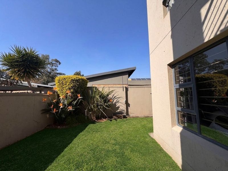 A well-maintained rear garden area featuring a manicured lawn, perimeter boundary walls with security spikes, and aluminium-framed windows with security bars.