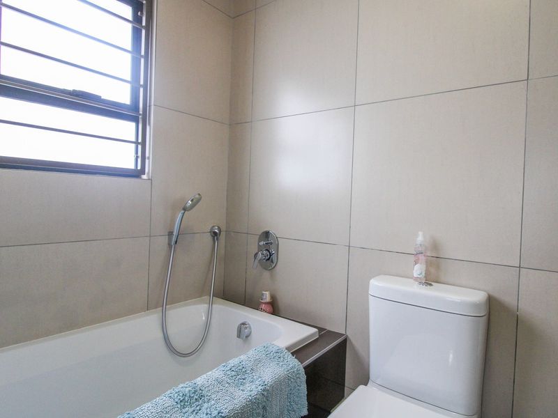 A functional bathroom featuring a built-in bathtub with a handheld shower mixer, a modern toilet, and neutral wall tiling.